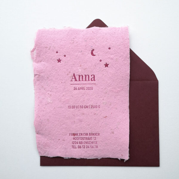 Geboortekaartje op roze handgeschept papier en een donkerrode envelop. De tekst is gedrukt in donkerrood en de kaart is versierd met sterren en een maantje.
