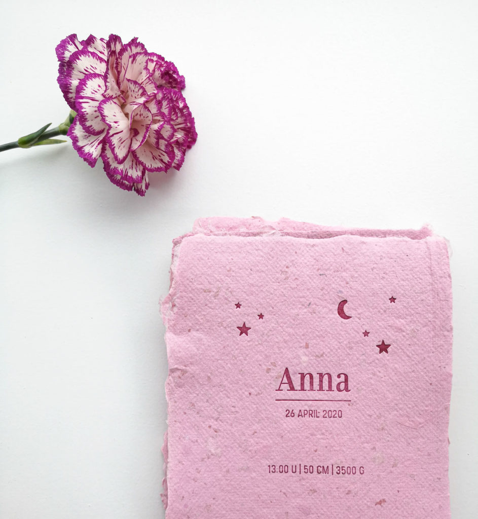 Geboortekaartje op roze, handgeschept papier met donkerrode tekst en een versiering met sterren en een maantje.