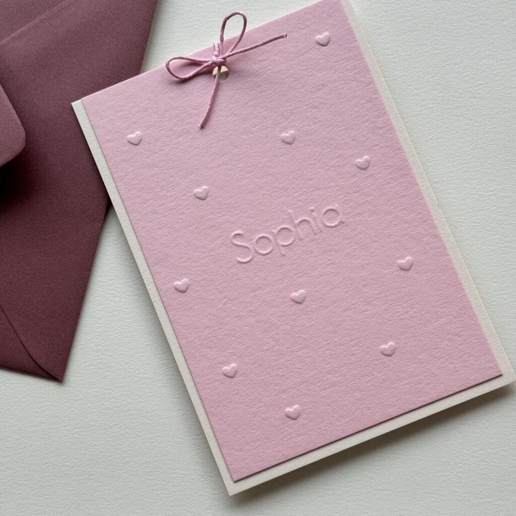 Een geboortekaartje op roze papier voor Sophia. Haar naam staat in het midden en is omringd door klein hartjes. Zowel haar naam als de hartjes zijn alleen in reliëf gedrukt.