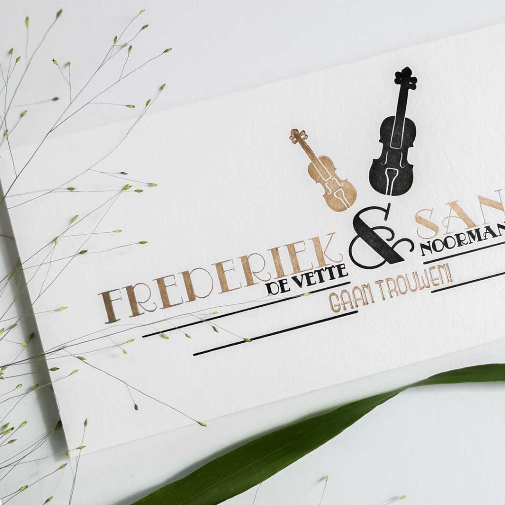 Close up van de trouwkaart van Frederiek en Sander. Met een viool en een cello gedrukt in goud en zwart.